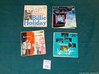 Four vintage record sleeves on a green surface: Billie Holiday's Lady Day, Sheena Easton album, a Willie Nelson record, and Red's Blue Room album.