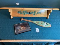 Overview photo of shelf, paddle, and framed artwork laid out on green cloth with measuring ruler for scale