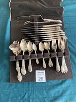 Set of silver plated cutlery laid out in a brown cloth holder showing various spoons, forks, and knives with detailed handles and an engraving letter B.