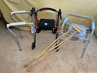 Full set of a collapsible walker, adjustable commode, toilet safety arms, and wooden crutches displayed on carpeted floor against a yellow backdrop.
