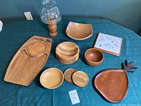 Wooden trays, bowls, coasters, ceramic tile trivet, and oil lamp arranged on table