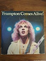 Front cover of 'Frampton Comes Alive!' vinyl album featuring Peter Frampton performing live on stage with lighting effects.