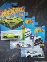 Three Hot Wheels toy cars in original packaging showing Aston Martin Vantage GTE, Chevy Impala, and Bentley Continental GT3 models.