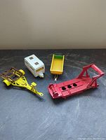 Four Matchbox trailers on a dark surface: red car transporter rig, white camper trailer, yellow utility trailer, yellow boat trailer.