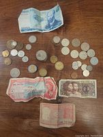 Photo showing assorted international currency coins and banknotes spread out on a wooden surface including a blue 10,000 denomination note and a red one dollar note with portraits