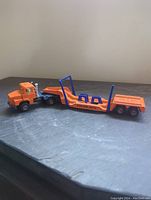 Side view of orange Majorette diecast toy truck rig with float trailer showing connection between truck and trailer and overall length.