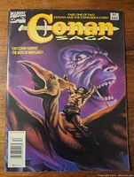 Front cover of the comic book showing Conan riding a dinosaur-like creature with a large face looming in the background showing the title and issue details
