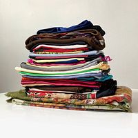 Side view of folded vintage scarves, handkerchiefs, pocket squares, neckerchiefs, and napkins stacked showing diverse colors and fabrics including some solid colors and patterns.