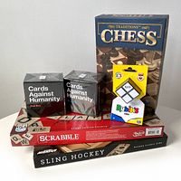 6 games displayed including Chess, Scrabble, Sling Hockey, Cards Against Humanity red and blue boxes, and Rubik's Mini cube puzzle.