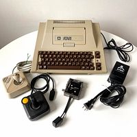 Atari 400 computer with keyboard and two joysticks, power adapter, and switch box laid out on table
