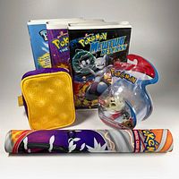Photo showing three Pokémon VHS movies in clamshells, a yellow zippered Pokéball Gameboy case, a rolled Pokémon playmat, and a sealed 2018 Pokémon 2-inch Battle Figure pack.