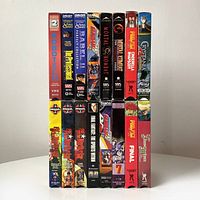 Side view showing the 16 stacked VHS tapes with colorful anime-themed spine artwork, including titles such as Robotech, Babel II, and Mortal Kombat.