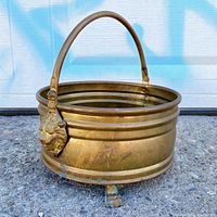 Side view of brass jardiniere showing lion head detail and paw feet with folding handle upright.