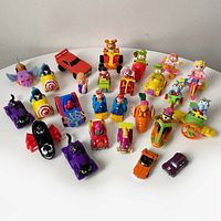 Photo showing collection of 26 plastic character toys on vehicles, featuring Batman, Spider-Man, Muppets, and more.