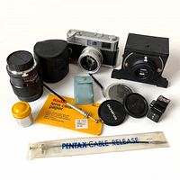 Photo showing all items in the vintage photography lot including camera, lenses, Kodak lens cleaning paper, blue container, cable release and others.