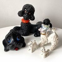 Photo showing the full lot of five poodle figurines including one large black poodle, one white poodle with bonnet, and three small white poodles.