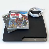Sony PlayStation 3 Slim console with two game cases and power cord on top showing overall lot contents.