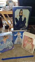 Four boxed Barbie dolls arranged standing on the floor including one in blue formal dress, Holiday Barbie, Birthday Barbie and one in light blue dress