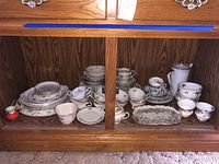 Full display of assorted fine china, including plates, teacups, bowls, coffee pot inside wood cabinet.