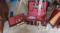 Full view of jewelry box with various necklaces draped over and several costume jewelry pieces inside including pins and earrings.