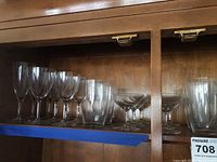 Photo showing five different types of crystal glasses arranged on a wooden shelf, highlighting the varied shapes and sizes.