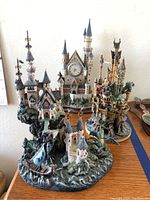 Three Danbury Mint collectible pieces: a clock castle and two castle sculptures with detailed bases including a dragon and sailing ship.