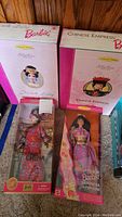 Photo showing boxed French Lady Barbie from The Great Eras Collection and Chinese Empress Barbie Collector Edition in upright pink boxes side by side with additional boxed Barbies in front.