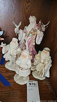 Five Lenox Christmas Santa Claus figurines on wooden surface including a larger pink and gold detailed Santa and four smaller white Santas with various holiday poses and objects.