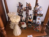 Photo showing 2 Lenox candleholders and 6 collectible Lenox figurines including Native American and Pilgrim characters on a wooden surface.