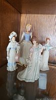 Four porcelain Lenox figurines including Cinderella in blue ball gown and other three figures in period dresses