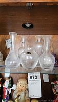 Four Lenox glass vases on glass shelf with etched floral designs visible