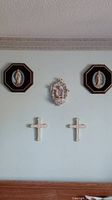 Wide shot showing all five pieces: two octagonal framed Virgin Mary reliefs, one central unframed religious plaque, and two white decorative crosses arranged on wall.