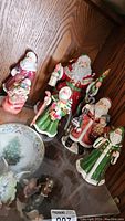 Group photo of all six Santa Claus figurines displayed on wood shelf.