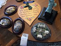 Four wall plaques including heart-shaped plaque with German text, three oval plaques with buildings, and a hexagonal plaque with white buildings. Statue of Liberty figurine also visible.