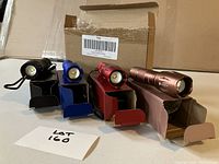 Four colorful flashlights in black, blue, red, and rose gold with their boxes displayed on a table.