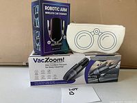Photo showing boxed robotic arm wireless car charger, VacZoom! mini cordless vacuum, and white zipped glasses case with binocular design.