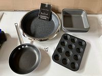 Top view of Curtis Stone 14-inch multipurpose pan with package/front label and other baking accessories: square baking pan, muffin pan, and frying pan