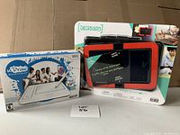 Lot includes two boxed electronic game tablets: a white uDraw GameTablet for Wii with included stylus and game, and a DashBoard digital drawing pad in black and orange with stylus, shown in packaging.