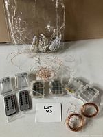 Nine strings of copper wire fairy lights with clear battery holders and two remote controls on white surface