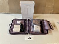 Clear cosmetic storage container with purple suede interior and multiple Monat cosmetics inside, alongside original boxes