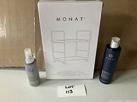 Vanity tray box next to two Monat branded cosmetic products: a spray labeled 'Rewind' and a dark blue squeeze bottle with white cap.