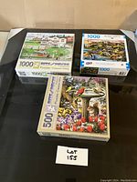 Three boxed jigsaw puzzles on a puzzle board with lot number card in view.