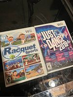 Photo showing the front covers of Racquet Sports and Just Dance 2018 games for Wii on a dark surface.
