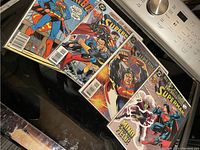 Photo shows four Superman comic books arranged side by side with visible front covers.