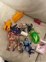 Photo showing the group of three He-Man figures including two He-Mans and one Skeletor, multiple small vehicles, plastic bugs and a collector card