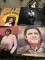 Four various vinyl record albums stacked showing album cover art including Johnny Cash, Marty Robbins, Julian Lennon, and an unidentified male artist.