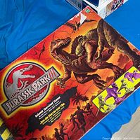 Top view of Jurassic Park Island Survival board game box showing colorful dinosaur artwork and game title.