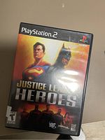 Front cover photo of Justice League Heroes for PlayStation 2 showing main characters Superman and Batman, along with logos for DC, Snowblind Studios, and Warner Bros.