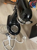 Black KitchenAid stand mixer base with two white mixing attachments next to it on the floor.