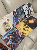 Eight vinyl record albums placed on a light colored couch, covers include artists of different genres including pop and rock